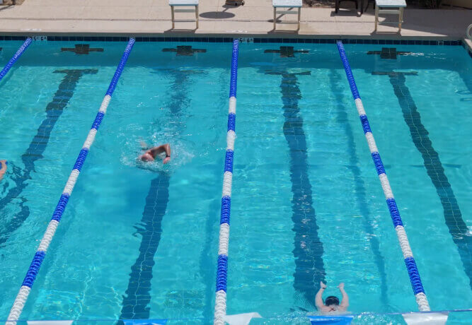 Village Clubs at DC Ranch aerial of a lap pool with three swimmers in lanes and two lounge chairs by the poolside.