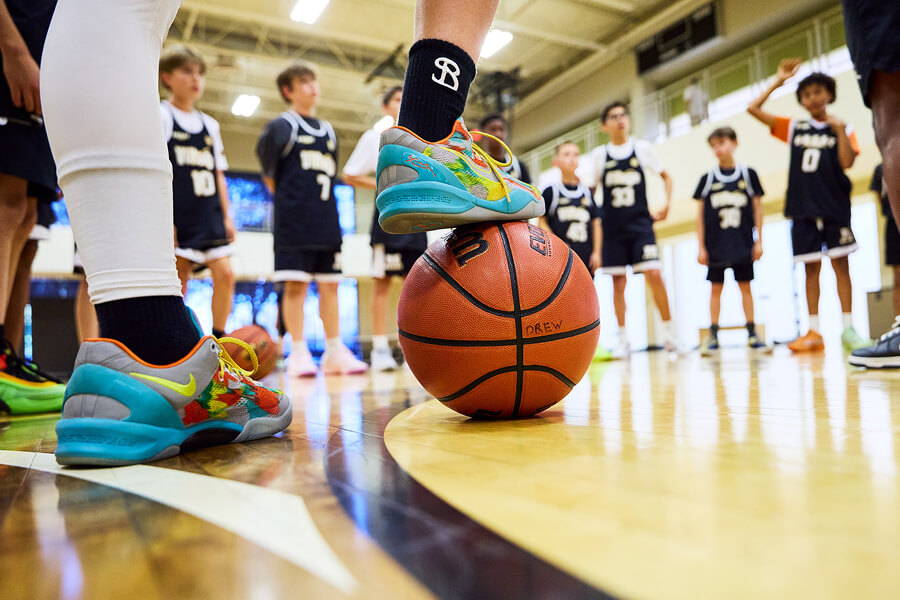 Close-up of Village Clubs Camelback youth basketball players in uniform, with colorful sneakers on a ball on the indoor court.