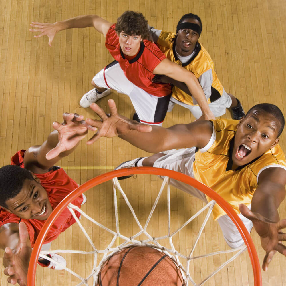 At Village Clubs Camelback, four basketball players leap near the hoop on a wooden court, reaching for the ball during game play.