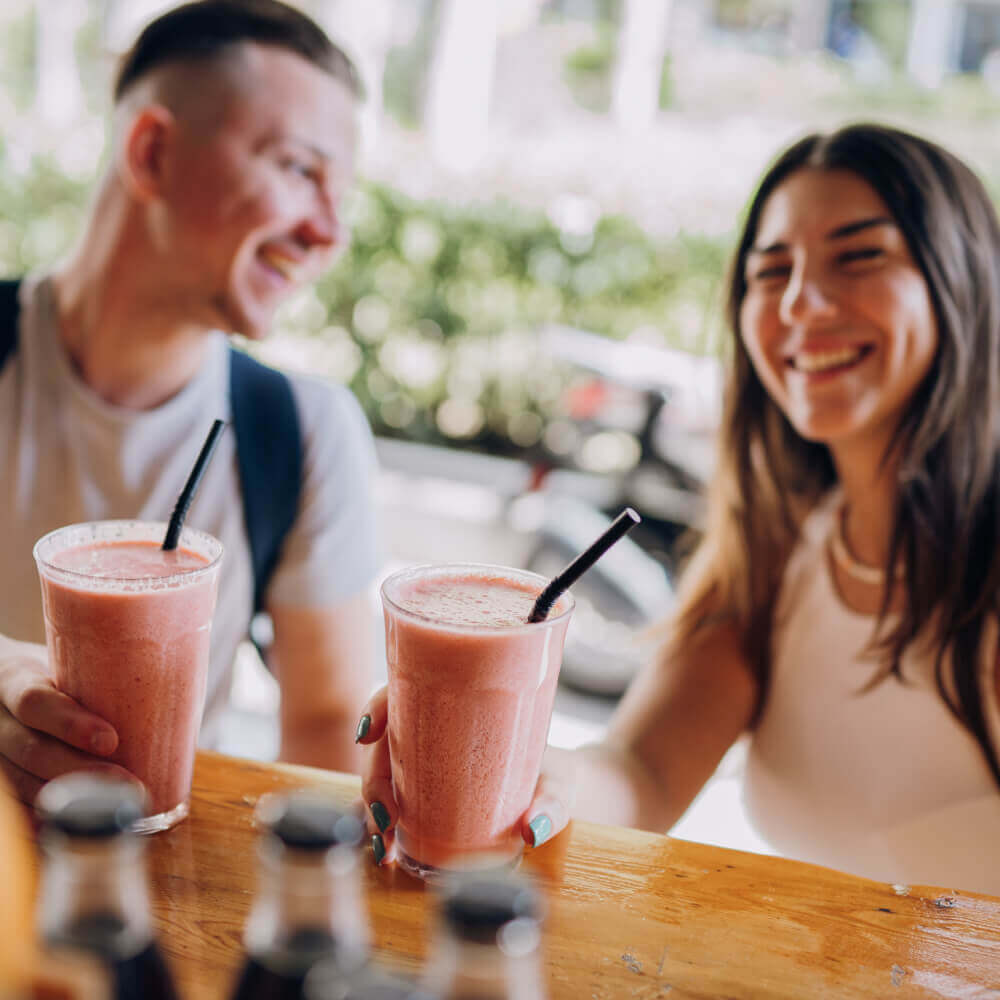 Guests at Village Clubs Camelback enjoy pink smoothies together at a bright café table, with bottles visible in the foreground.