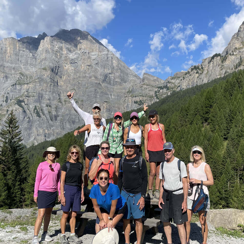 Village Clubs hikers at Camelback enjoy a sunny day outdoors, smiling with rocky mountains and tall pines in the background.