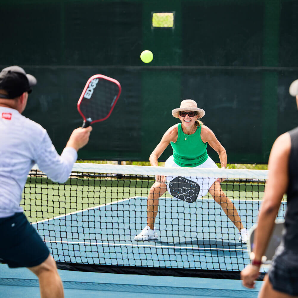 Village Clubs members play pickleball at Camelback in Arizona; a woman prepares by the net as two men return the ball mid-game.