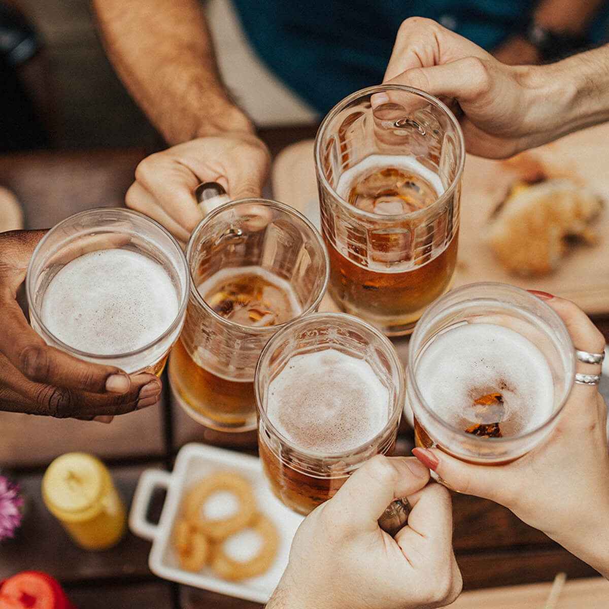 Members at Village Clubs Camelback toast with beer mugs over a table of food, celebrating at a lively social event.