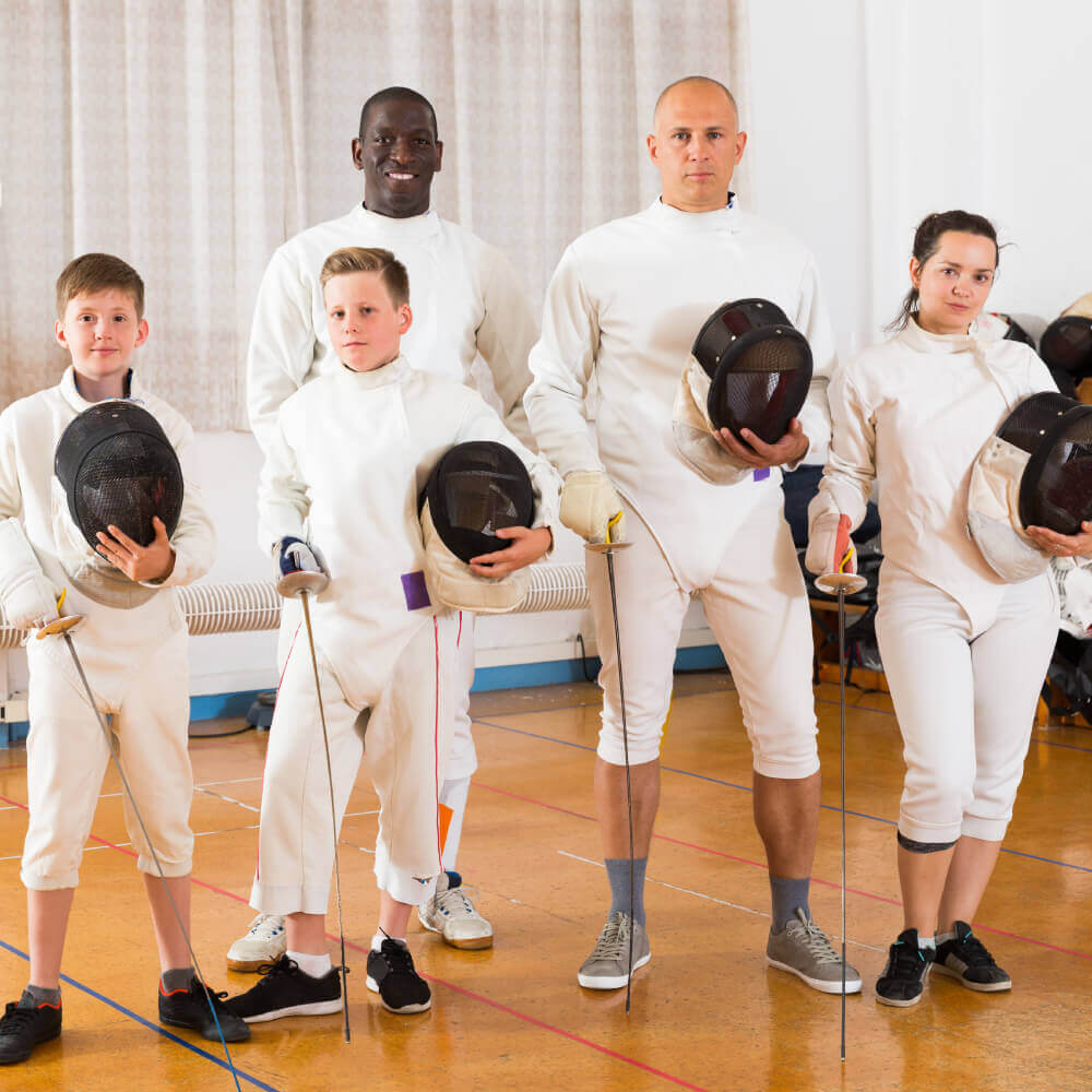 Members at Village Clubs Camelback enjoy indoor fencing, as three kids and two adults pose with masks and swords for a group photo.