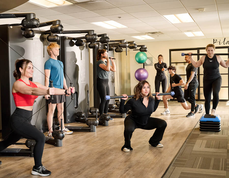Focused group fitness class working out at Village Clubs Camelback, lifting weights and using gym equipment in a bright studio.