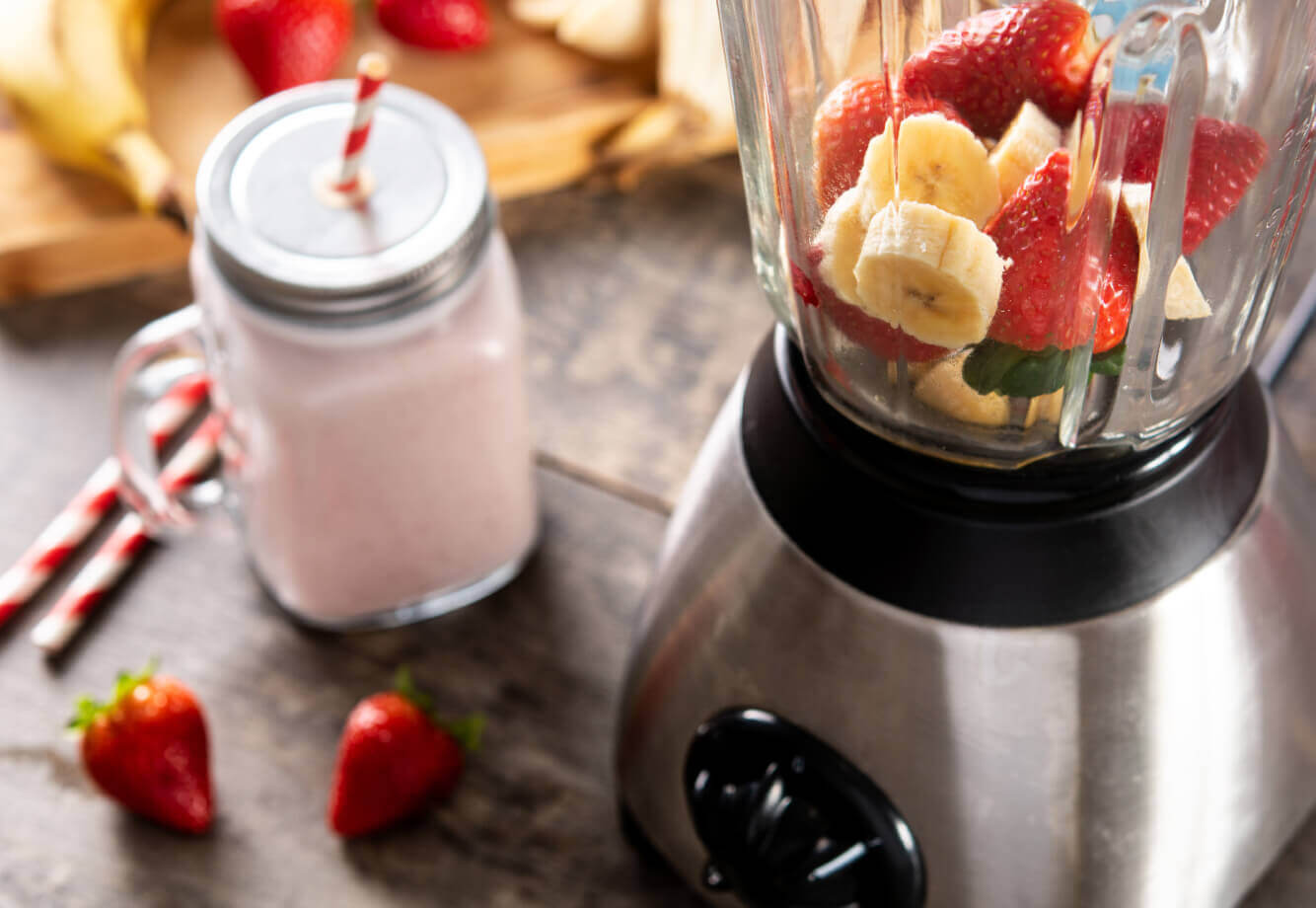 Village Clubs Camelback: Blender with fresh bananas, strawberries, and smoothie on wood table, highlighting healthy nutrition options.