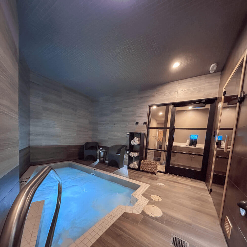 Village Clubs Camelback spa room with illuminated hot tub, lounge chairs, fresh towels, and glass doors to more relaxing amenities.