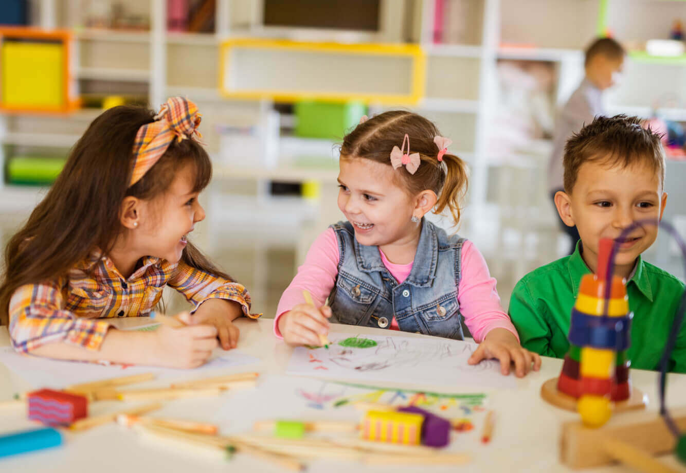 Children at Village Clubs Camelback enjoying art activities with colored pencils, blocks, and toys on a bright, kid-friendly table.