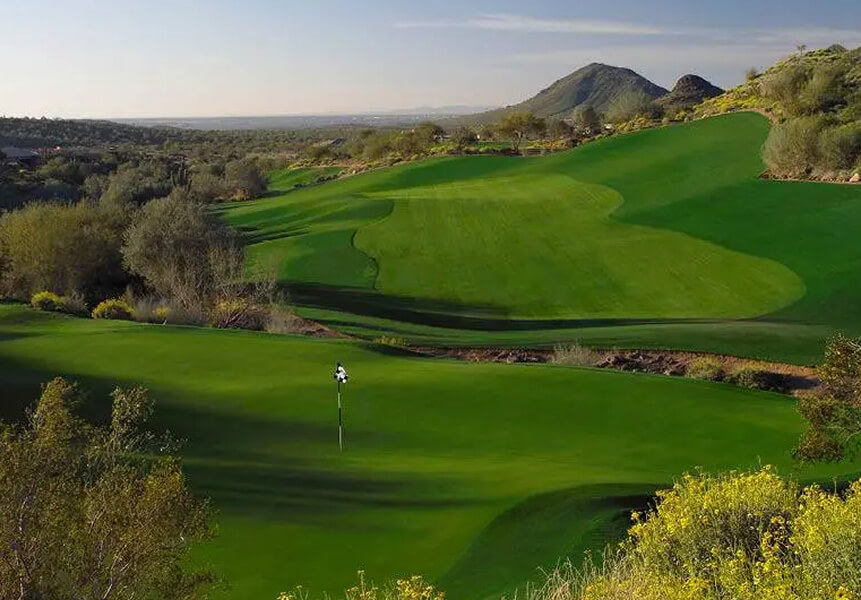 Village Clubs Camelback golf course features lush fairways, pristine greens, desert landscaping, distant hills, and clear skies.