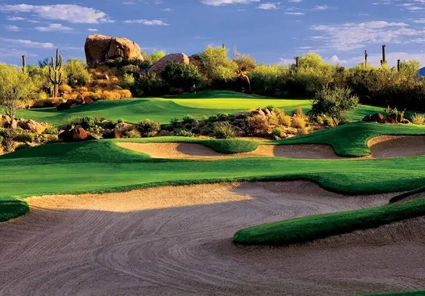 Village Clubs at Camelback golf course with lush fairways, sand bunkers, desert plants, and cacti beneath a partly cloudy sky.