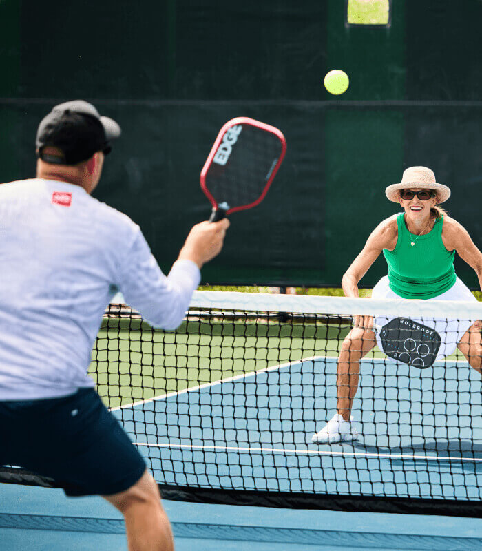 Two adults play pickleball at Village Clubs Camelback outdoor courts, with both players focused and ready for the next shot.