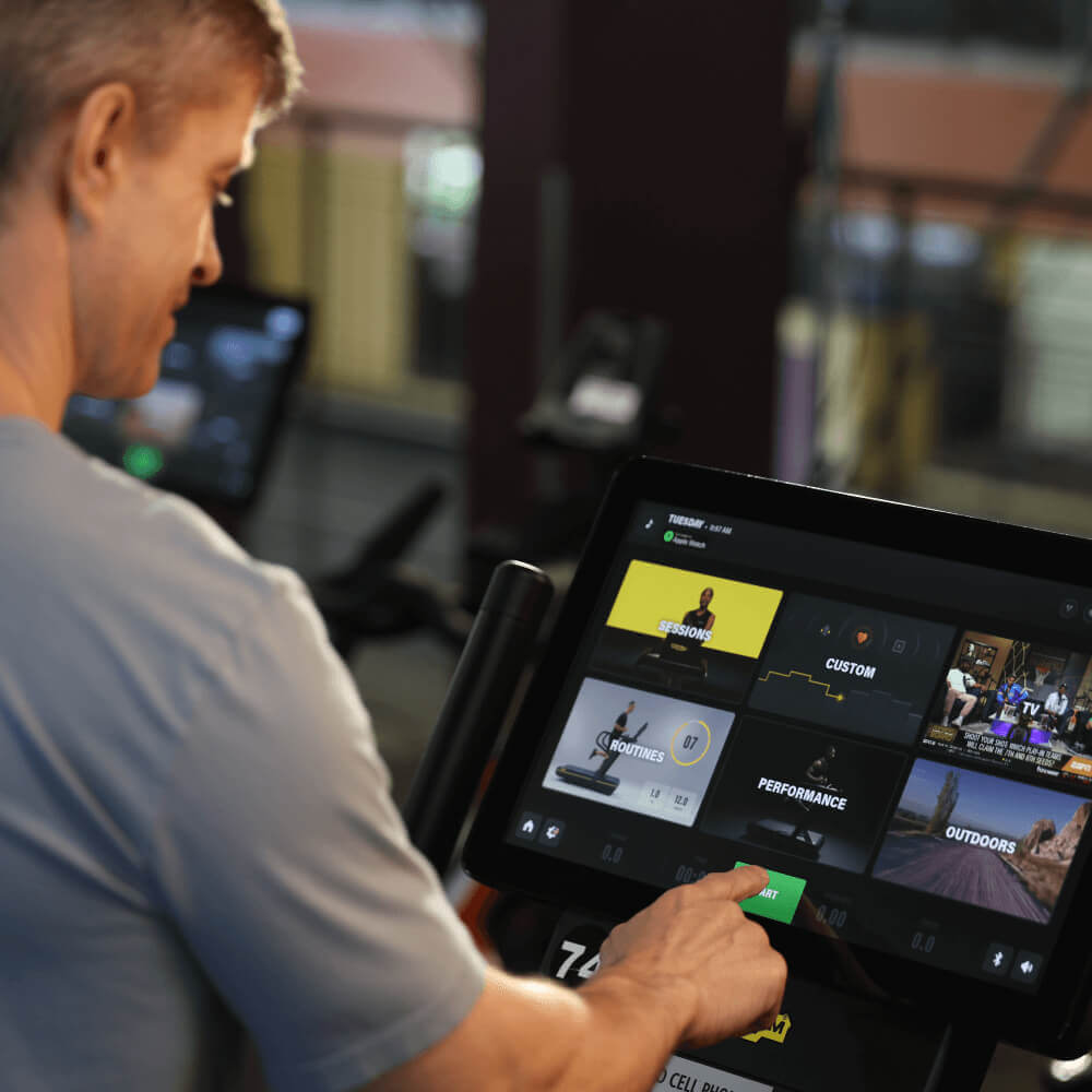 At Village Clubs Camelback, a gym member selects from custom workouts on a touchscreen, enjoying exclusive member perks.