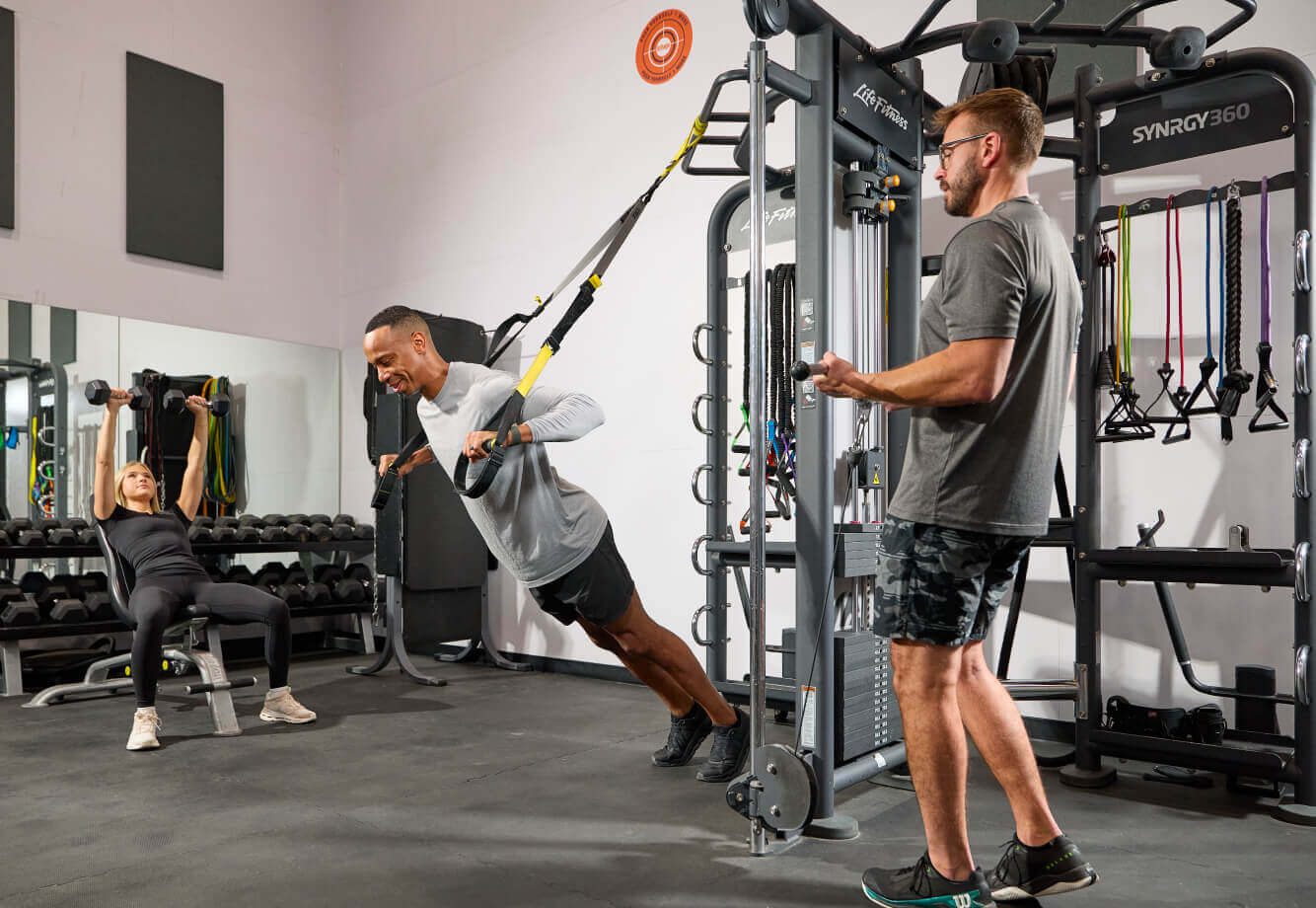At Village Clubs Camelback, members enjoy personal training with TRX, gym machines, and dumbbells in a modern fitness center.