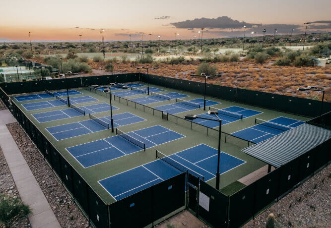 Aerial view of Village Clubs Camelback outdoor pickleball courts at sunset, with blue and green courts and desert scenery.