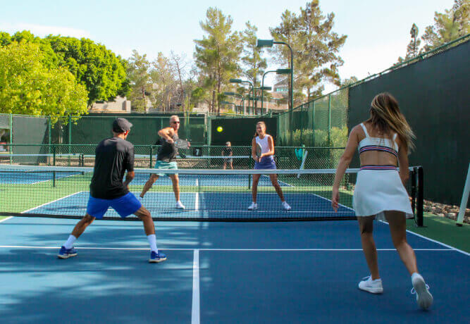 Members play doubles pickleball at Village Clubs Camelback in Arizona, focused on the ball under sunny skies on outdoor courts.