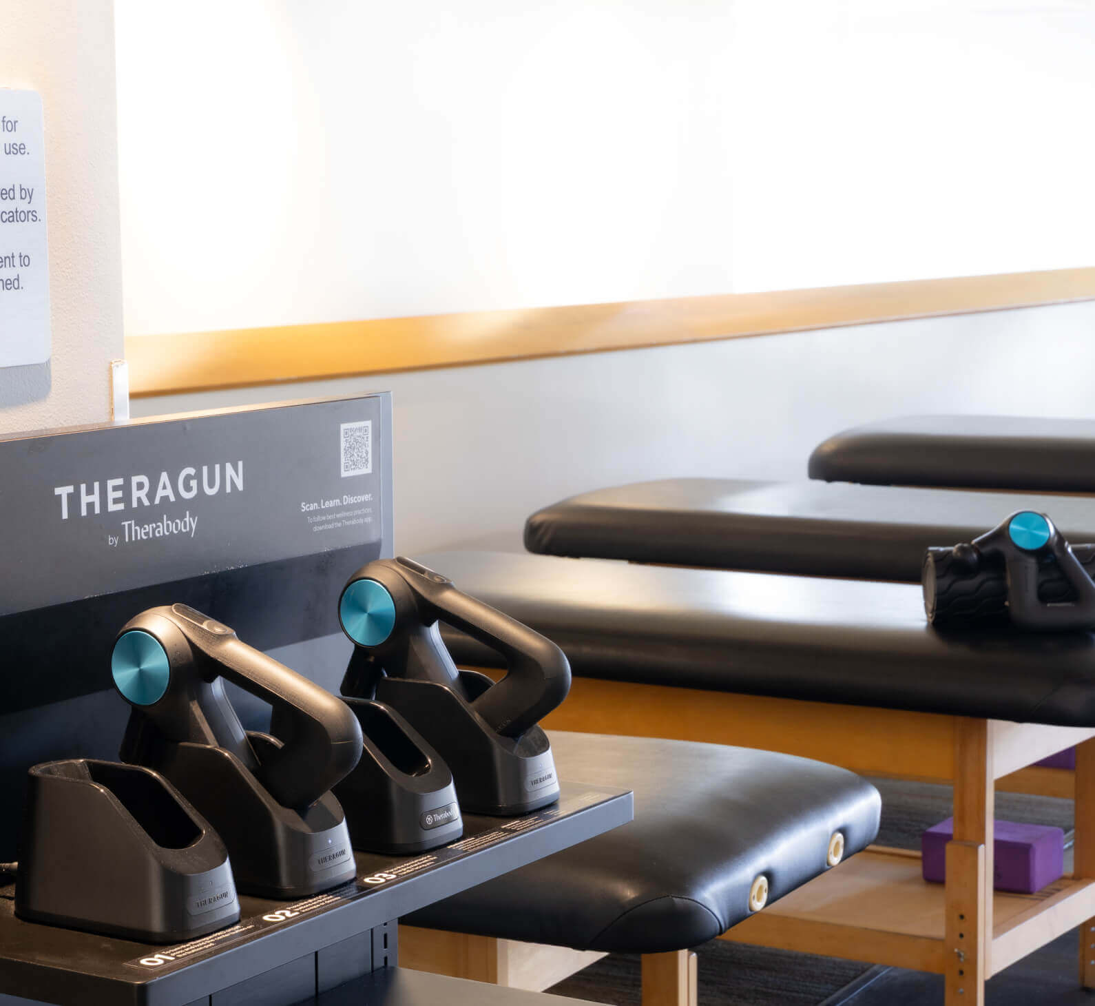 Theragun massage devices ready on a charging stand in a bright Village Clubs Camelback therapy room for recovery sessions.