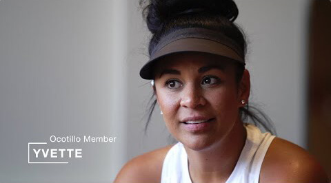 Village Clubs member Yvette at Ocotillo location, sitting indoors in a white sleeveless top and black visor.