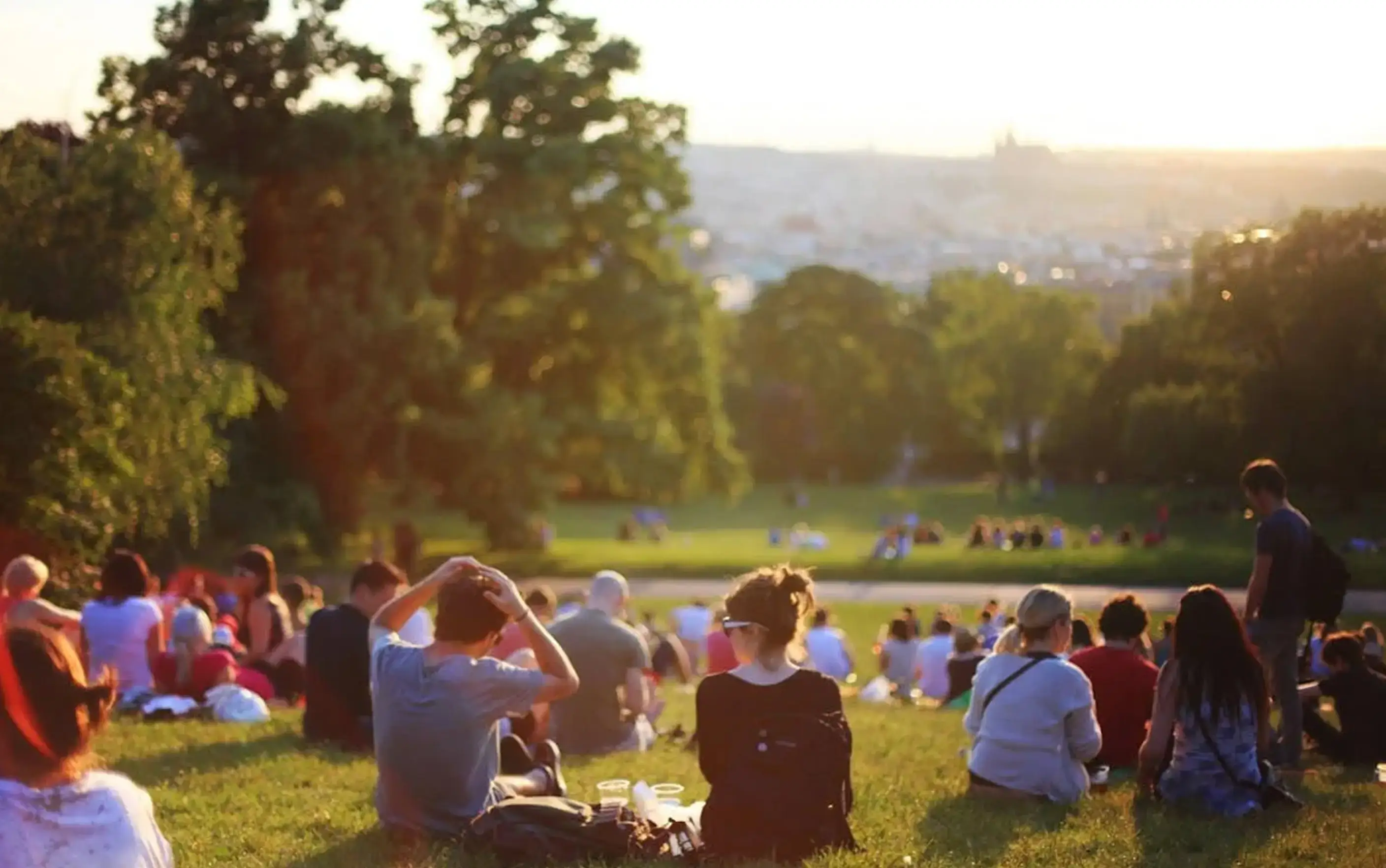 Members gather on a grassy hillside at Village Clubs Camelback, enjoying sunset and community programs with city views in the park.